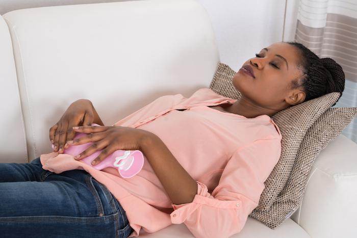 Woman lying on her back, applying a hot compress to her lower abdomen for pelvic pain relief.