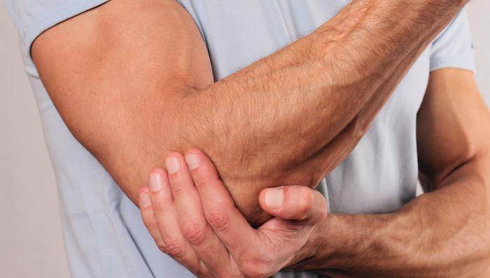 Man grips elbow, a sign of Tennis Elbow and Golfer's Elbow discomfort.