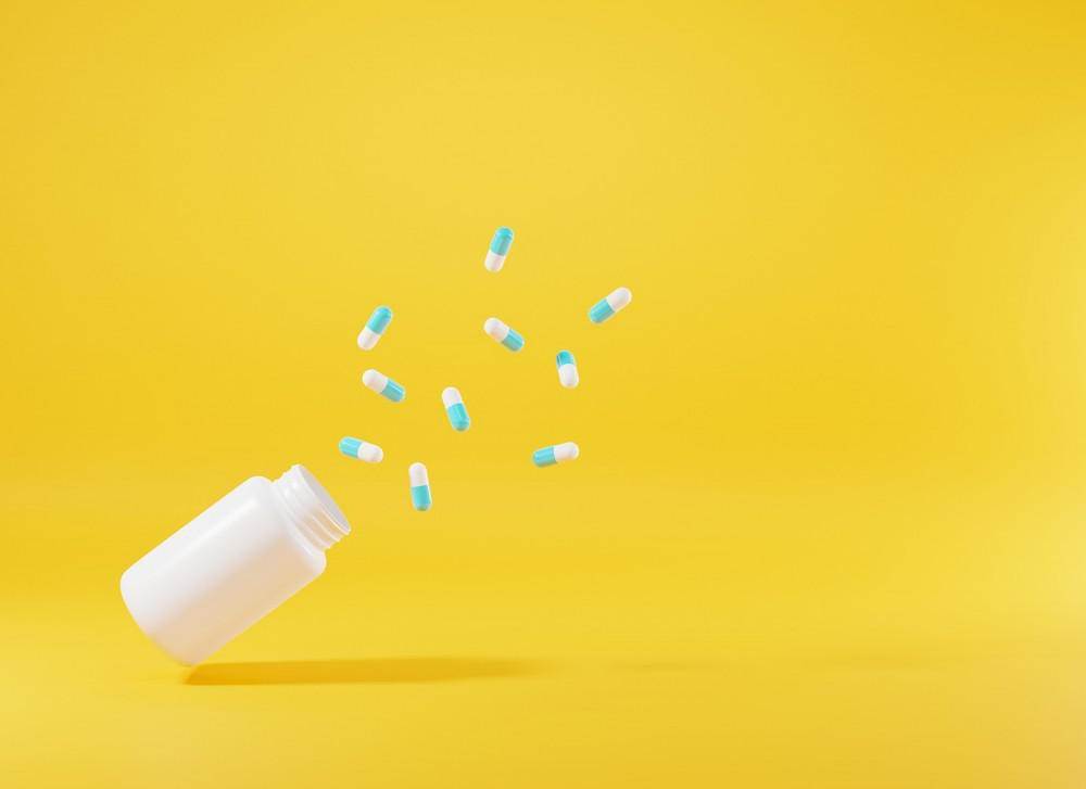 Pills spilling from a bottle on yellow, hinting at medication management.