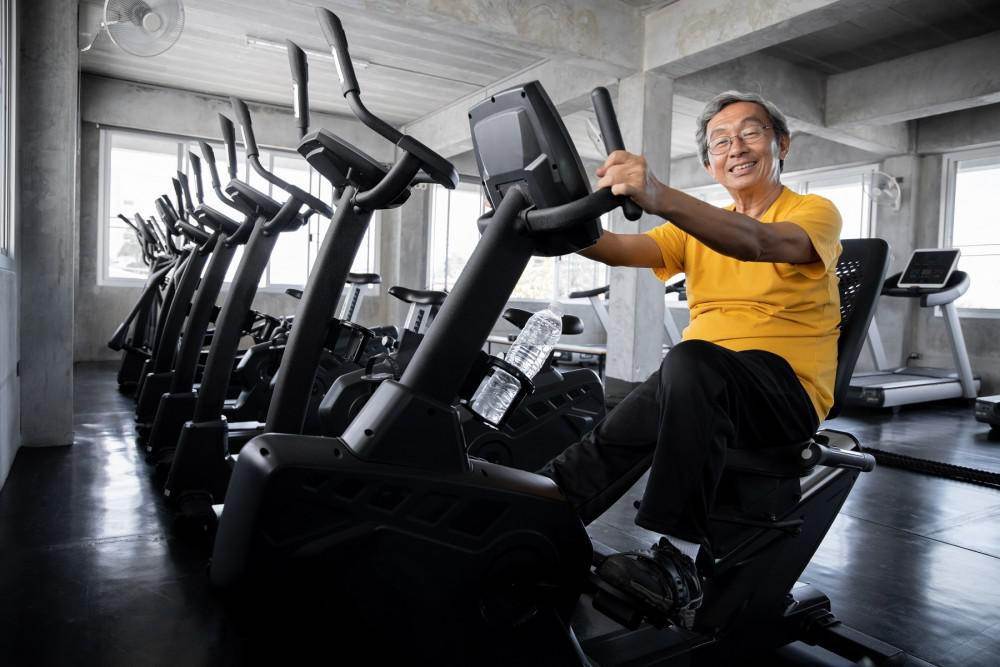 Senior man cycling in gym, showcasing active living to slow Progression of Osteoarthritis